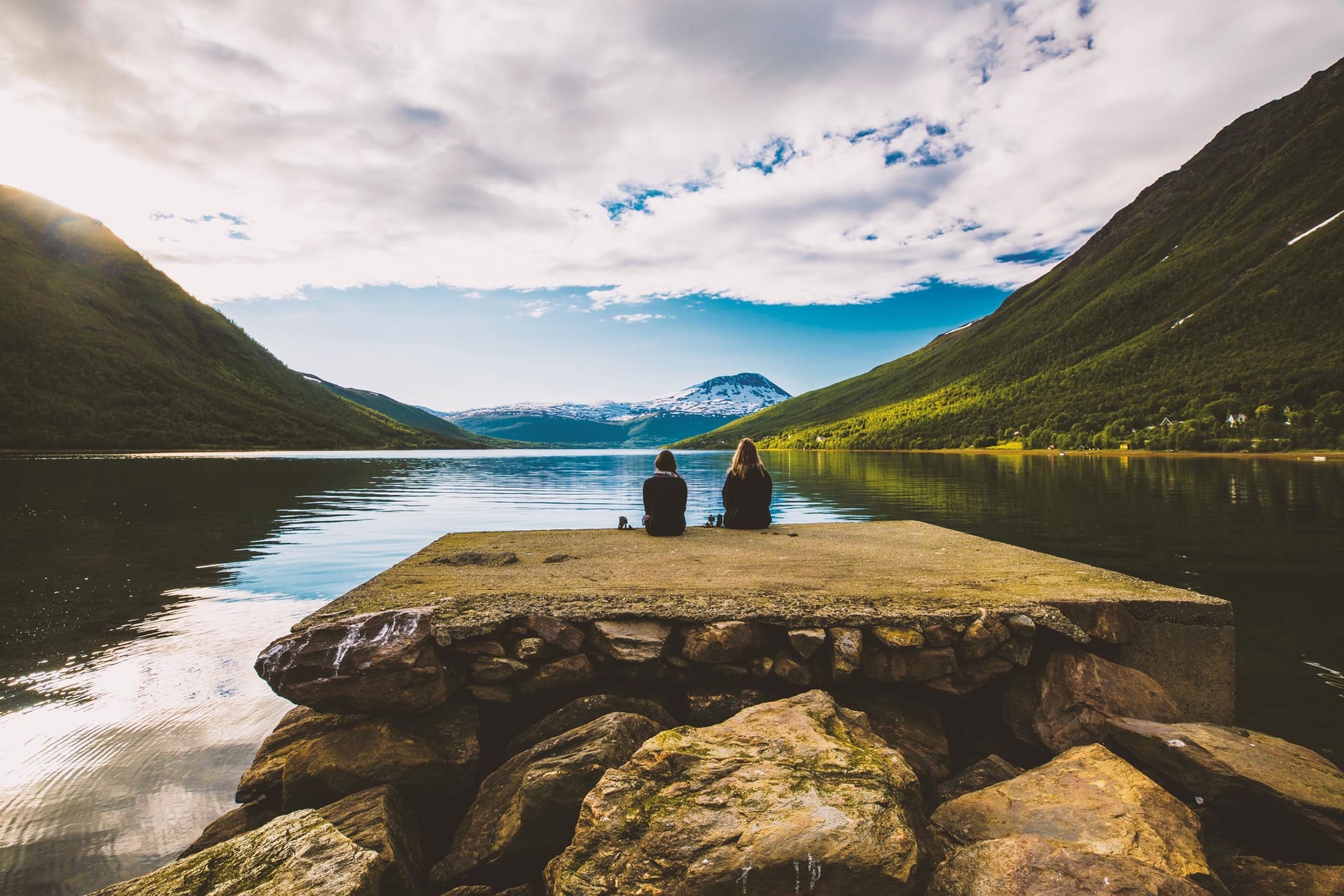 Two people sitting on a stone pier by a fjord in Norway