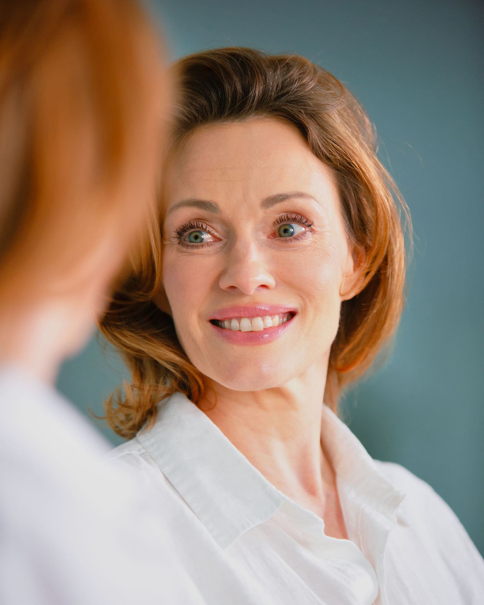 Krista Soltin smiling into a mirror against a blue-green wall