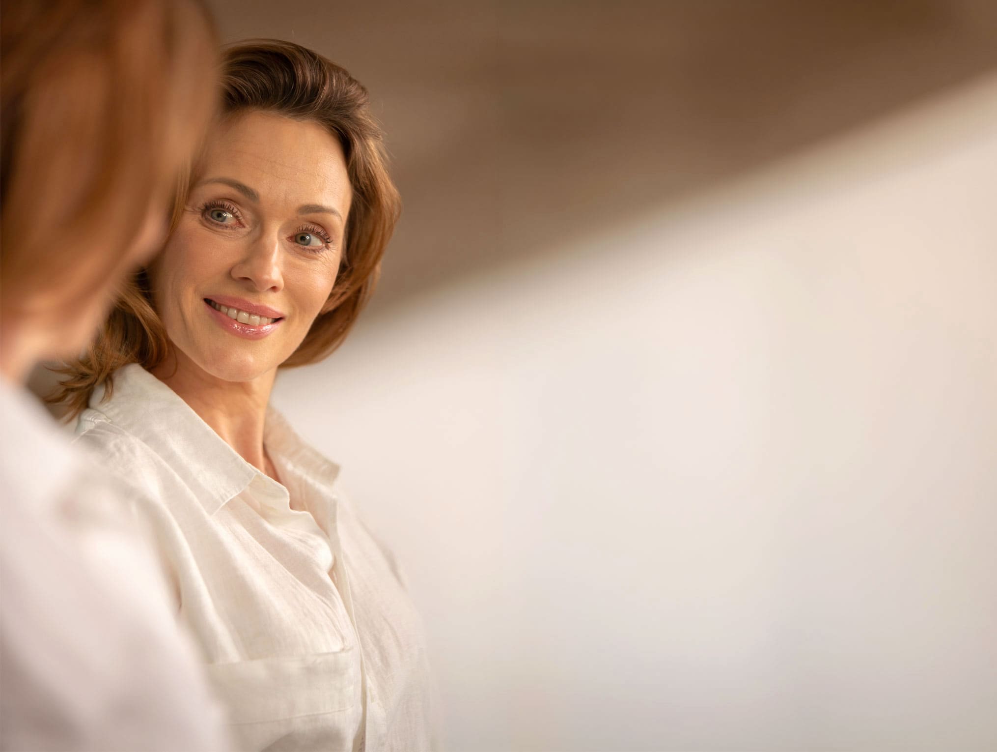 Krista Soltin in a white shirt smiling at her reflection, warm light on a pale wall